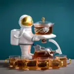 Un astronaute en plastique blanc portant un casque doré, tenant un plateau avec un récipient contenant un liquide marron, entouré de plusieurs tasses en verre avec un liquide similaire.