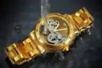 Montre mécanique dorée avec mouvement visible, immergée dans l'eau, mettant en valeur son design sophistiqué et ses détails techniques. Parfaite pour une décoration scientifique élégante.