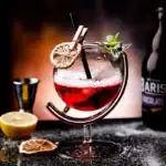 Verre de cocktail scientifique avec garniture de citron, menthe et paille, sur un fond sombre avec accessoires de bar.