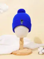 Bonnet en laine bleu avec un petit logo d'astronaute brodé, orné d’un pompon en laine. Parfait pour les amateurs de science et de style décontracté.