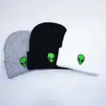 Trois casquettes en tissu gris, noir et blanc avec un logo extraterrestre vert, parfaites pour un style décontracté ou geek.