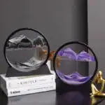 Panneau décoratif en verre avec montagnes en relief, suspendu dans un cadre circulaire noir, créant un effet visuel captivant.