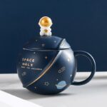Tasse décorative en forme de vaisseau spatial avec un petit astronaute en haut, décorée de motifs planétaires et étoiles, idéale pour les amateurs d'astronomie et de décoration scientifique.