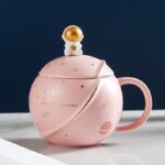 Vase décoratif en forme de tasse à thé avec motif spatial, comprenant un couvercle avec un petit astronaute doré. Parfait pour une décoration originale sur un bureau ou une étagère.