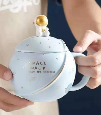 Tasse en céramique avec motif spatial et figurine d'astronaute doré sur le couvercle, idéale pour la décoration ou la consommation de boissons inspirées de l'espace.