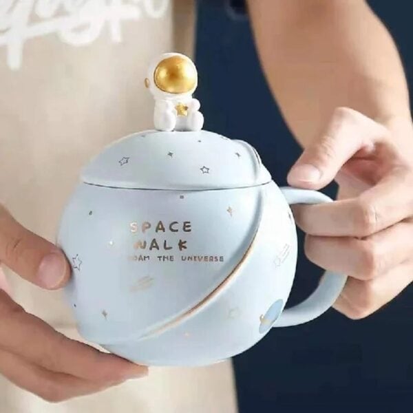 Tasse en céramique avec motif spatial et figurine d'astronaute doré sur le couvercle, idéale pour la décoration ou la consommation de boissons inspirées de l'espace.