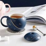 Tasse en céramique bleue avec motifs d'astres, accompagnée d'une souris d'ordinateur assortie, sur un bureau blanc avec un livre ouvert en arrière-plan.