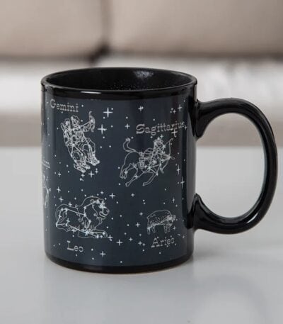 Mug en céramique noir avec illustrations des constellations du zodiaque : Gémeaux, Sagittaire, Lion, Bélier, et plus, avec noms en français.