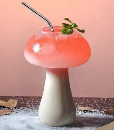 Verre en forme de champignon contenant un cocktail rose avec une branche de menthe, décoratif et original.