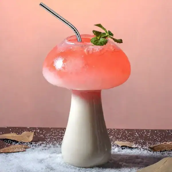 Verre en forme de champignon contenant un cocktail rose avec une branche de menthe, décoratif et original.