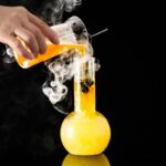 Manipulation d'une expérience scientifique avec un liquide orange fumant dans un laboratoire, utilisant un bécher et un tube à essai, contre un fond noir.