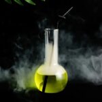 Vase de laboratoire contenant un liquide fluorescent jaune avec un tube en verre et de la fumée autour, évoquant une expérience scientifique mystérieuse.
