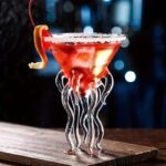 Cocktail rouge dans un verre en forme de méduse avec tentacules en verre, garniture d'orange et glace, sur une surface en bois, ambiance nocturne et mystérieuse.