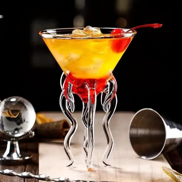 Verre à cocktail scientifique avec décor en forme de tentacules en verre transparent, rempli d'un cocktail jaune-orange avec cerise, ambiance de bar moderne.