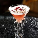 Cocktail rose dans un verre en forme de flacon avec décorations florales.