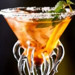 Verre à cocktail avec garniture de menthe et citron, décoré avec du sel sur le rebord, mettant en valeur une boisson colorée et rafraîchissante.