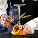 Flacon de laboratoire avec liquide orange, décoré de blé et d'une cuillère, illustrant la science et la recherche.