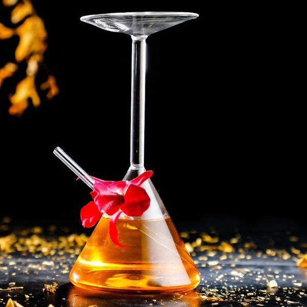 Béchier de laboratoire avec verre à cocktail suspendu, contenant un liquide orange, décoré d'une fleur rouge, sur une surface noire avec des éclats dorés.