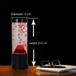 Vase à bulles de savon avec lumière LED rouge, hauteur 25,5 cm et diamètre 9 cm, posé sur une table en bois avec des lunettes et un carnet à côté, fond noir.
