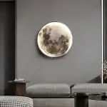 Décoration murale représentant la lune en relief, illuminée, dans un intérieur moderne avec canapé gris et table basse.