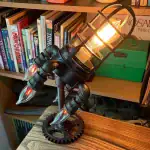 Lampe de bureau design inspirée d'une fusée avec éclairage chaud et structure métallique noire. Parfaite pour une décoration moderne ou thématique scientifique.