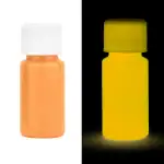 Pillules fluorescentes orange et jaune sous lumière noire, illustrant la fluorescence dans un environnement sombre.