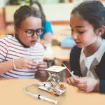 Deux jeunes filles explorent un robot éducatif scientifique lors d'une activité en classe, illustrant l'apprentissage ludique de la technologie et de la robotique pour les enfants.