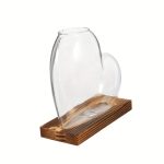 Vase en verre transparent en forme de cœur, posé sur un socle en bois naturel, idéal pour la décoration scientifique ou artistique.