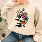 Sweatshirt avec motif de microscope entouré de fleurs colorées, parfait pour les amateurs de science et de décoration originale.
