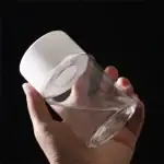Verre à cocktail transparent avec couvercle en silicone blanc, tenu par une main, sur fond noir.